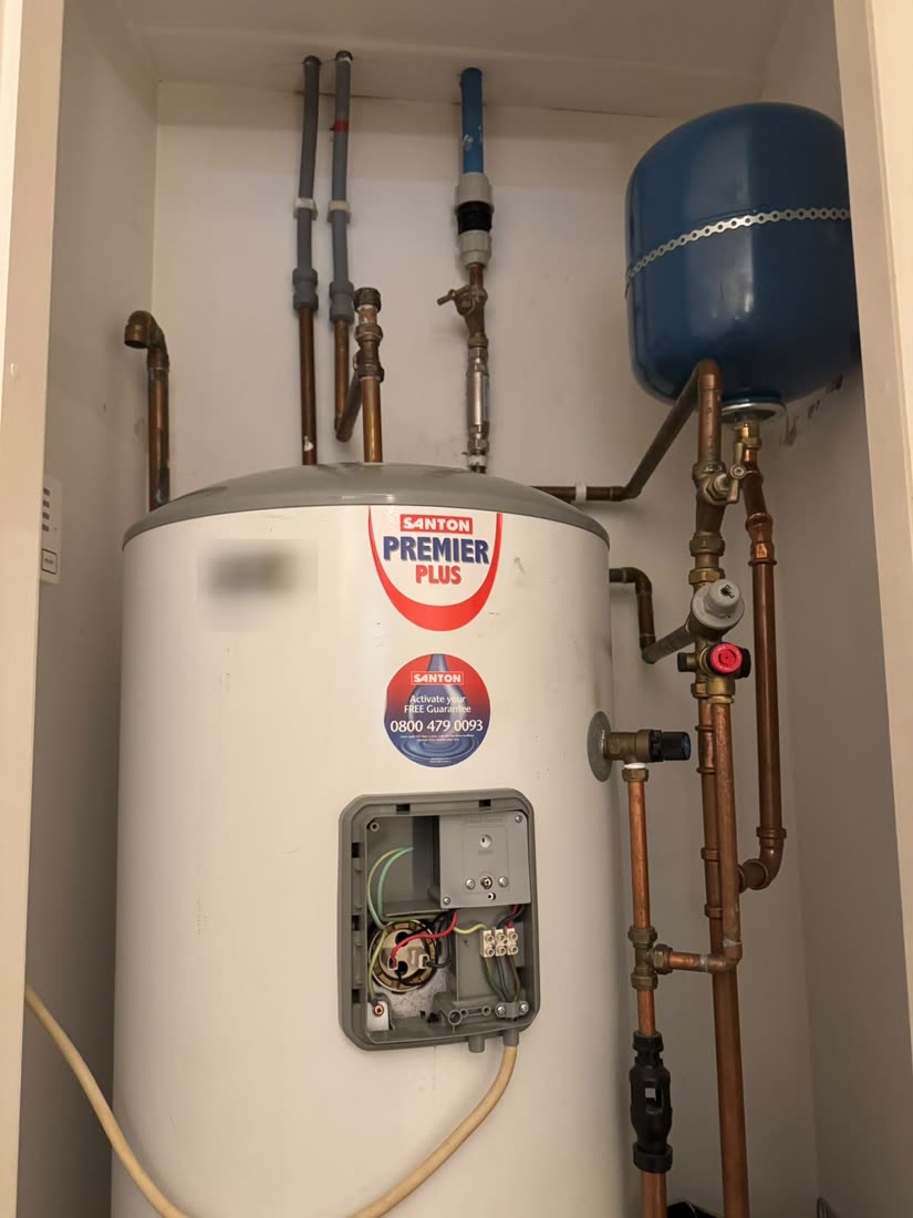 Unvented hot water cylinder in an airing cupboard during a repair, showing the expansion vessel, valve set and pipework